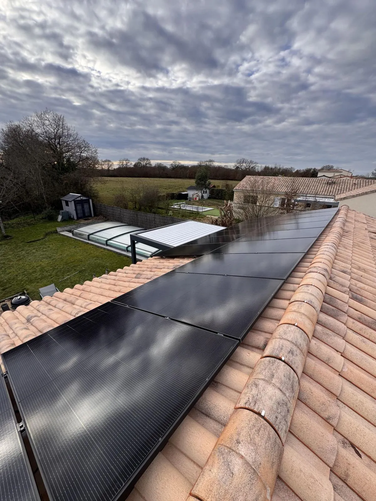 Toit en tuiles équipé de panneaux, piscine couverte visible dans le jardin