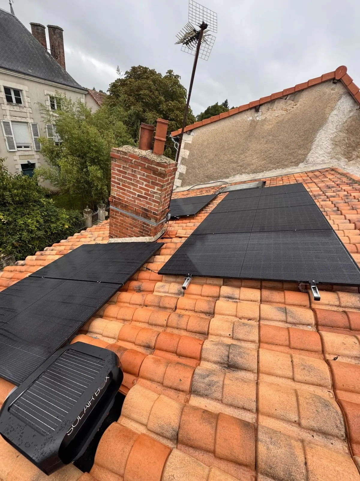 Panneaux solaires posés de part et d'autre d'une cheminée sur un toit en tuiles canal